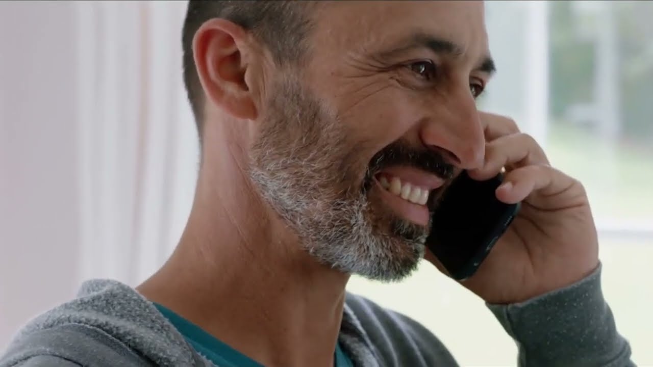 A Houston homeowner smiling on the phone after a RoofSquad roof inspection